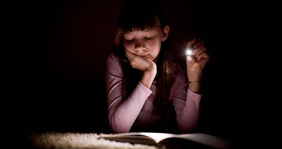 girl reading in the dark with a flastlight